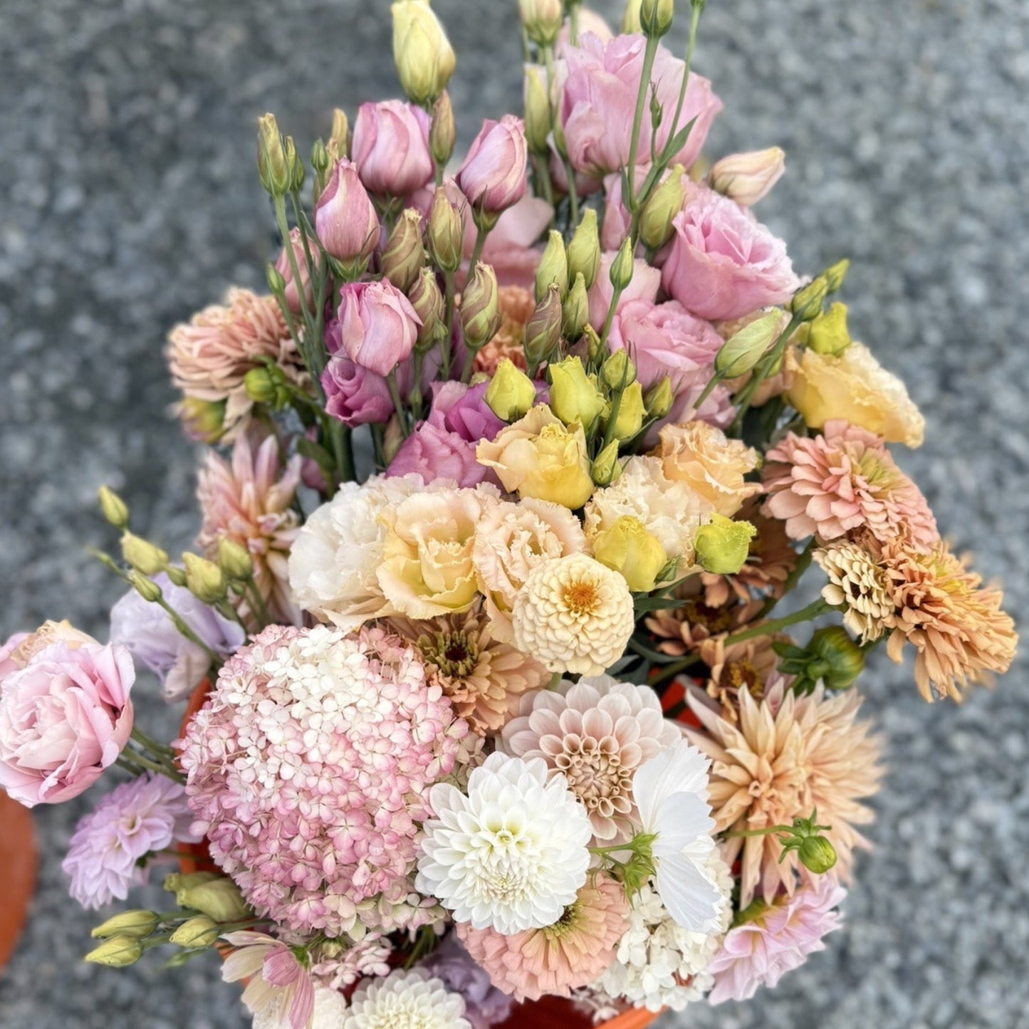 Colorful bouquet of flowers in an orange pot on a gray pavement.