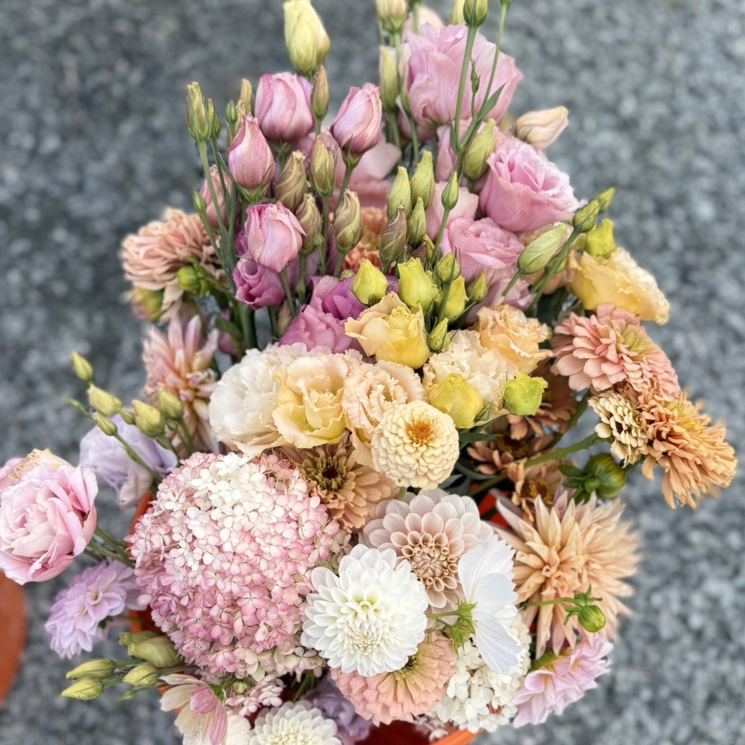 Colorful bouquet of flowers in an orange pot on a gray pavement.