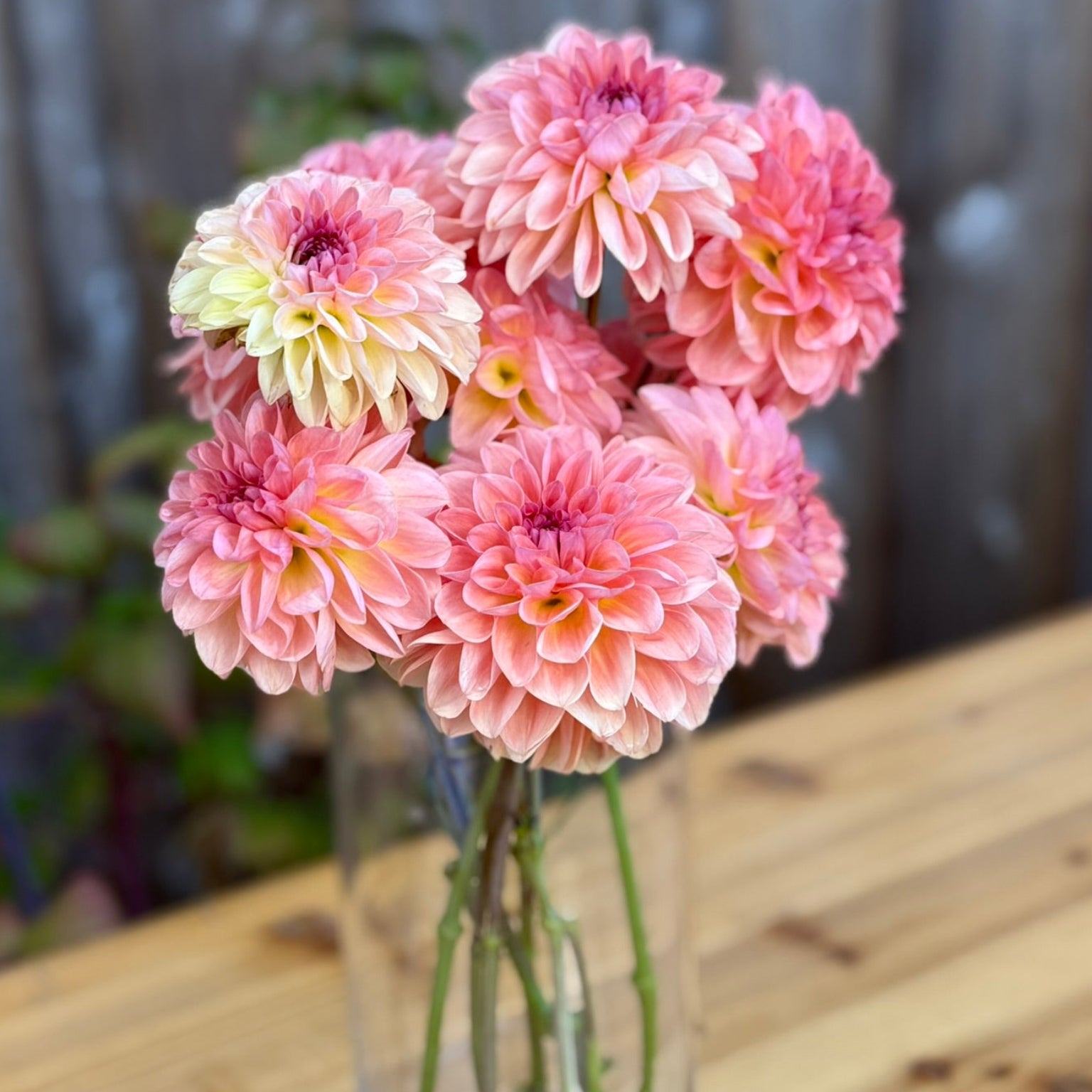 Bouquet of pink and yellow flowers in a clear vase on a wooden table.